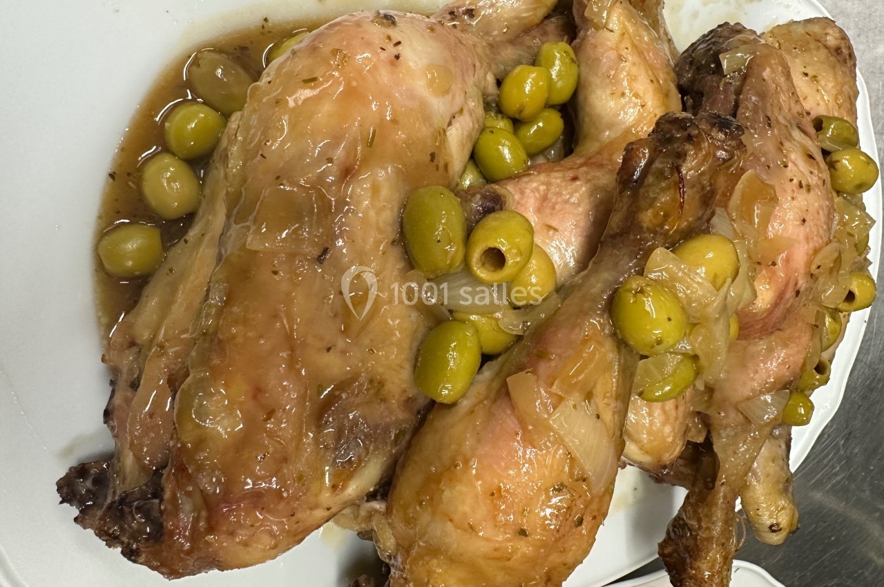 Poulet rôti nappé de sauce aux oignons et olives vertes, présenté sur une assiette blanche.