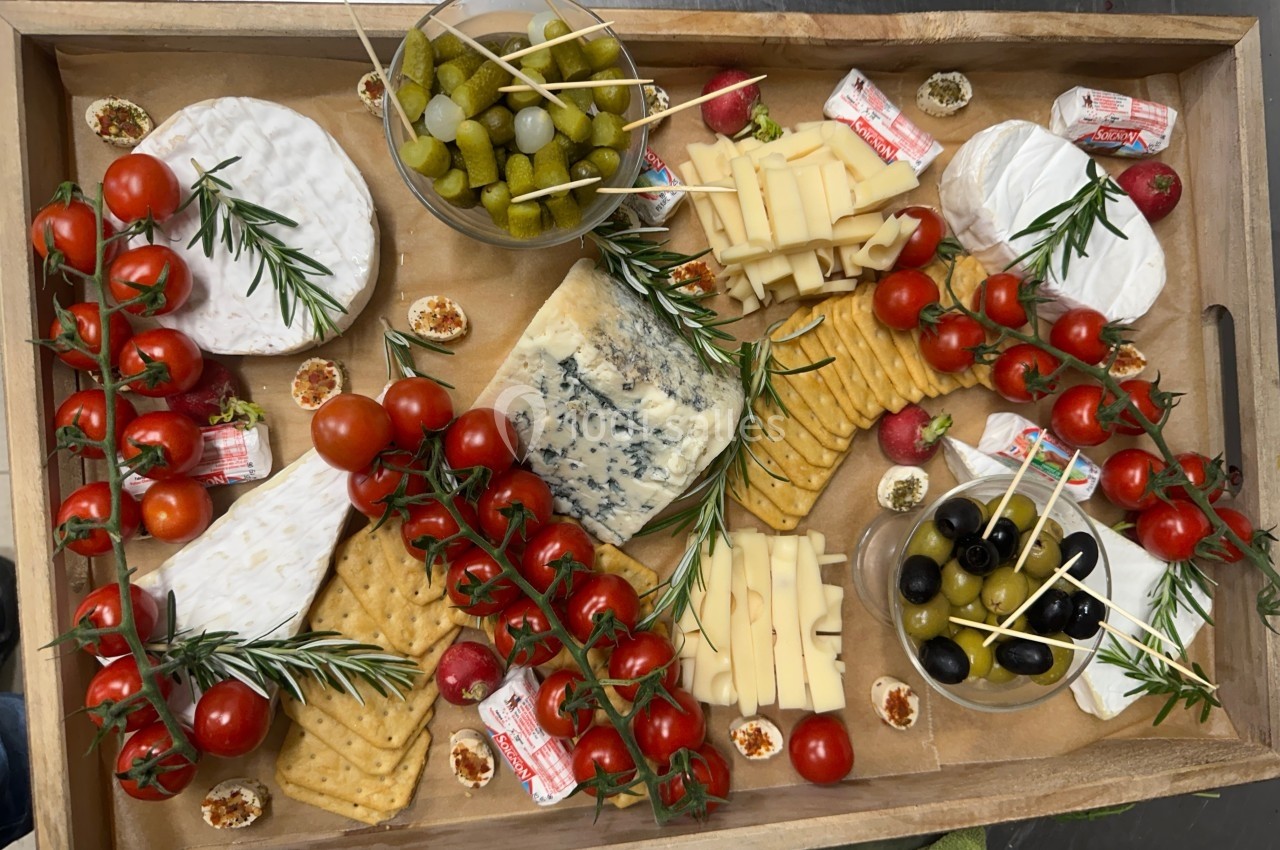 Plateau en bois garni de fromages variés, tomates cerises, olives, cornichons, crackers et brins de romarin.