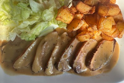 Assiette contenant un steak grillé, une purée de pommes de terre, une salade verte et une sauce servie dans un ramequin.