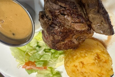 Assiette contenant un steak grillé, une purée de pommes de terre, une salade verte et une sauce servie dans un ramequin.