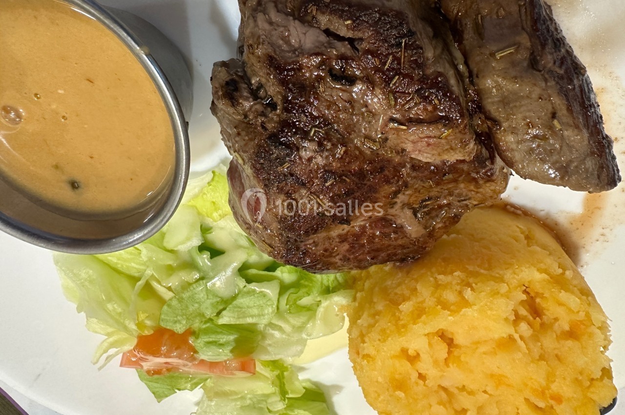 Assiette contenant un steak grillé, une purée de pommes de terre, une salade verte et une sauce servie dans un ramequin.