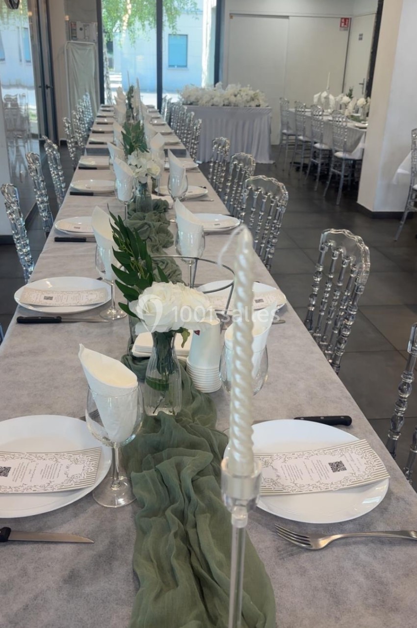 Grande table de réception décorée avec une nappe grise, un chemin de table vert, des fleurs blanches et de la vaisselle…