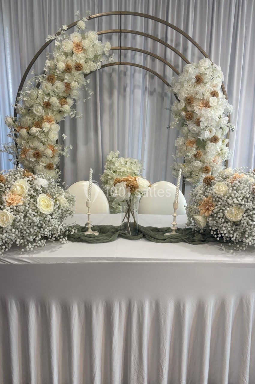 Table décorée pour un mariage avec des fleurs blanches et beige, bougies et arche florale en arrière-plan.