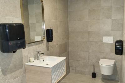 Toilettes modernes avec cuvette suspendue, carrelage gris, mosaïque dorée et accessoires noirs.