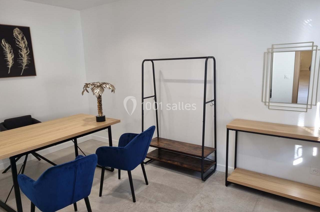 Salle minimaliste avec table en bois, chaises bleues, étagère métallique, miroir mural et décoration murale.