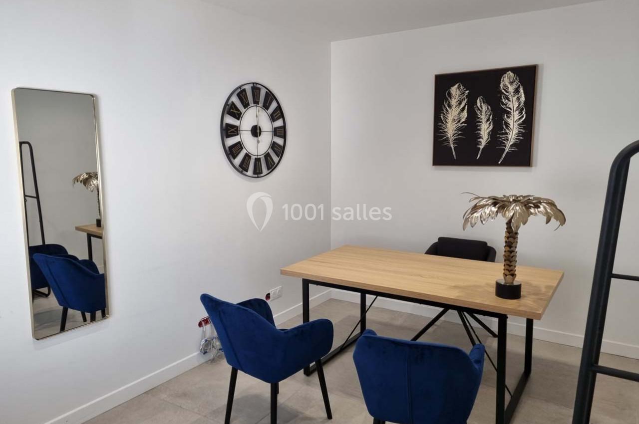Bureau moderne avec table en bois, chaises bleues, miroir, horloge murale et décoration murale de plumes dorées.