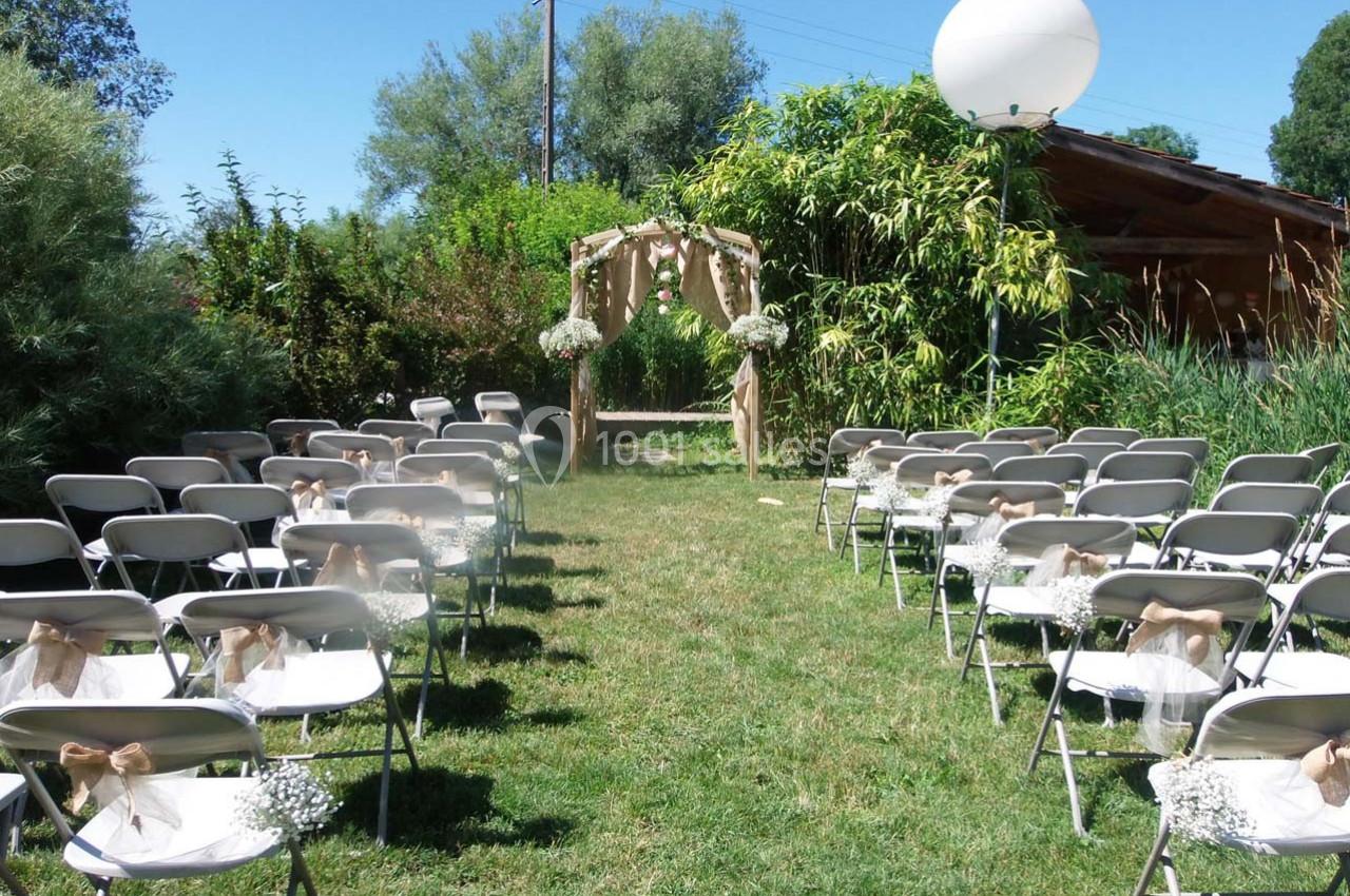 Chaises alignées sur une pelouse face à une arche décorée de fleurs, préparées pour une cérémonie en plein air.