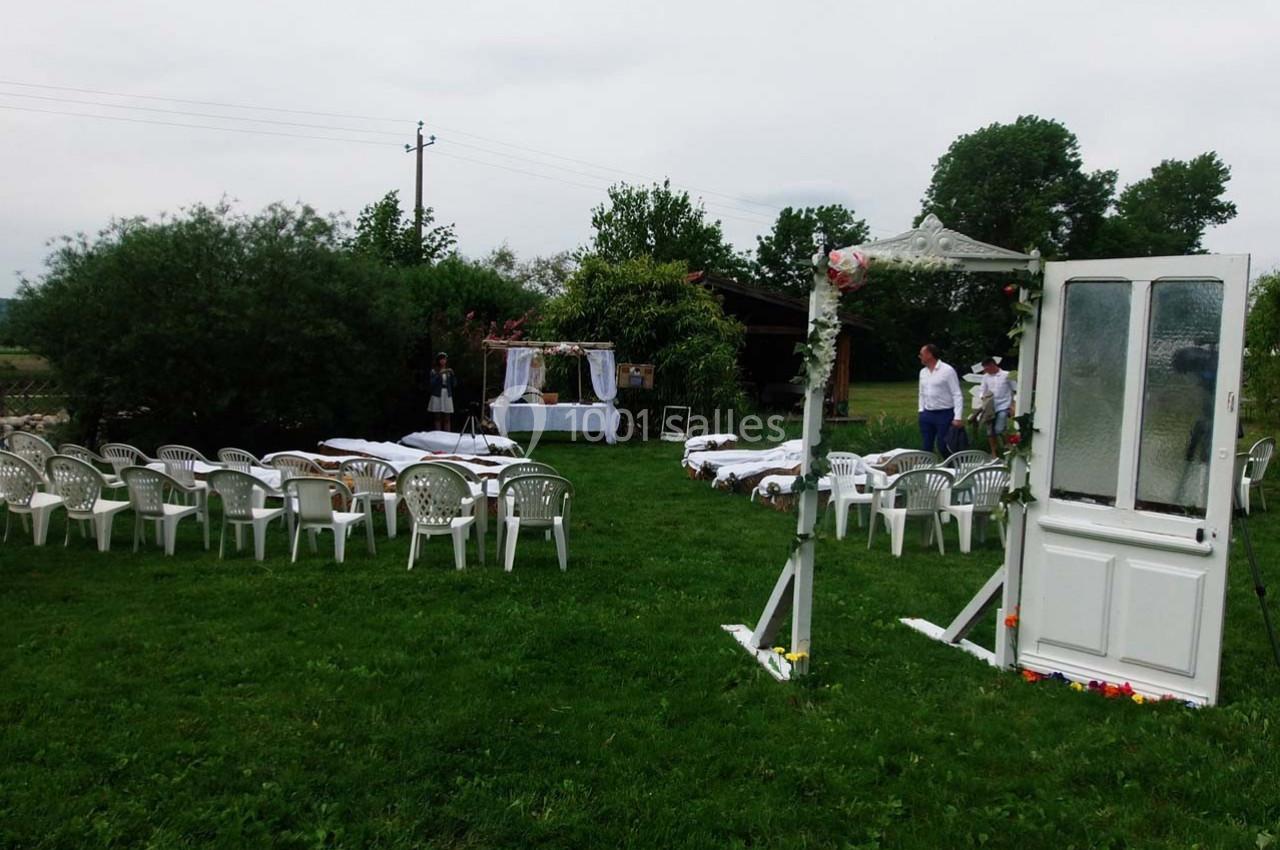 Chaises blanches disposées en extérieur sur une pelouse, face à une arche décorée pour une cérémonie.