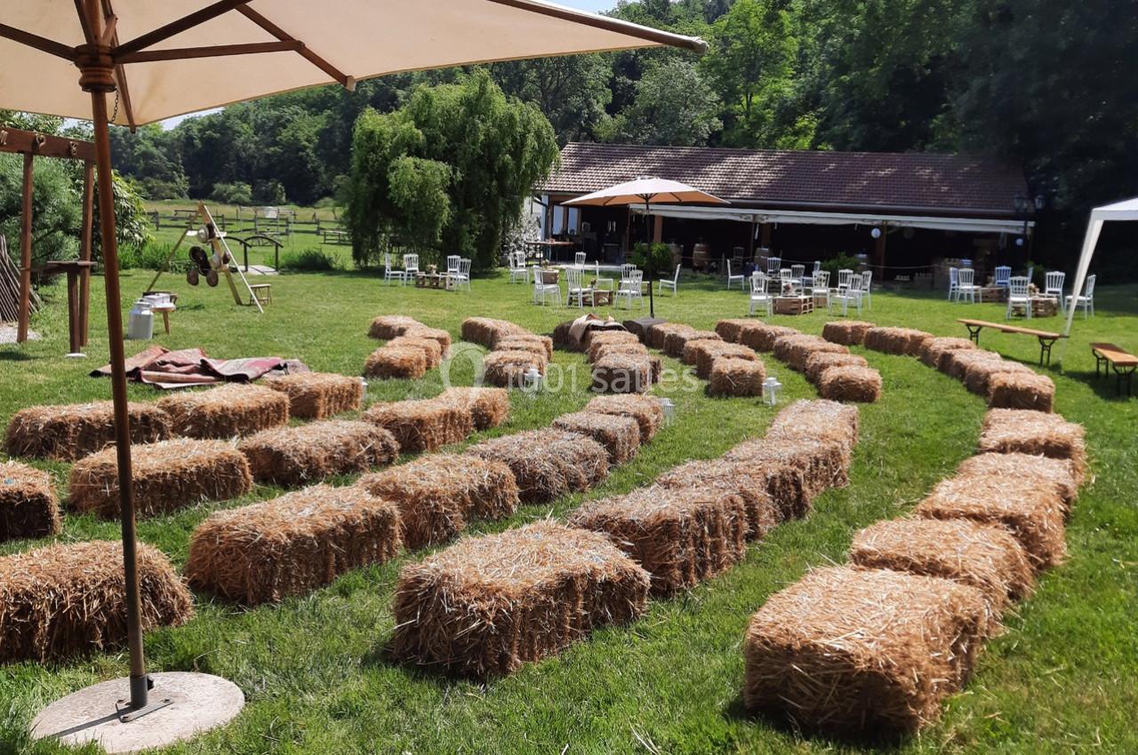 Bottes de paille disposées en rangées sur une pelouse, formant un espace assis en plein air près d'un bâtiment et d'arbres.