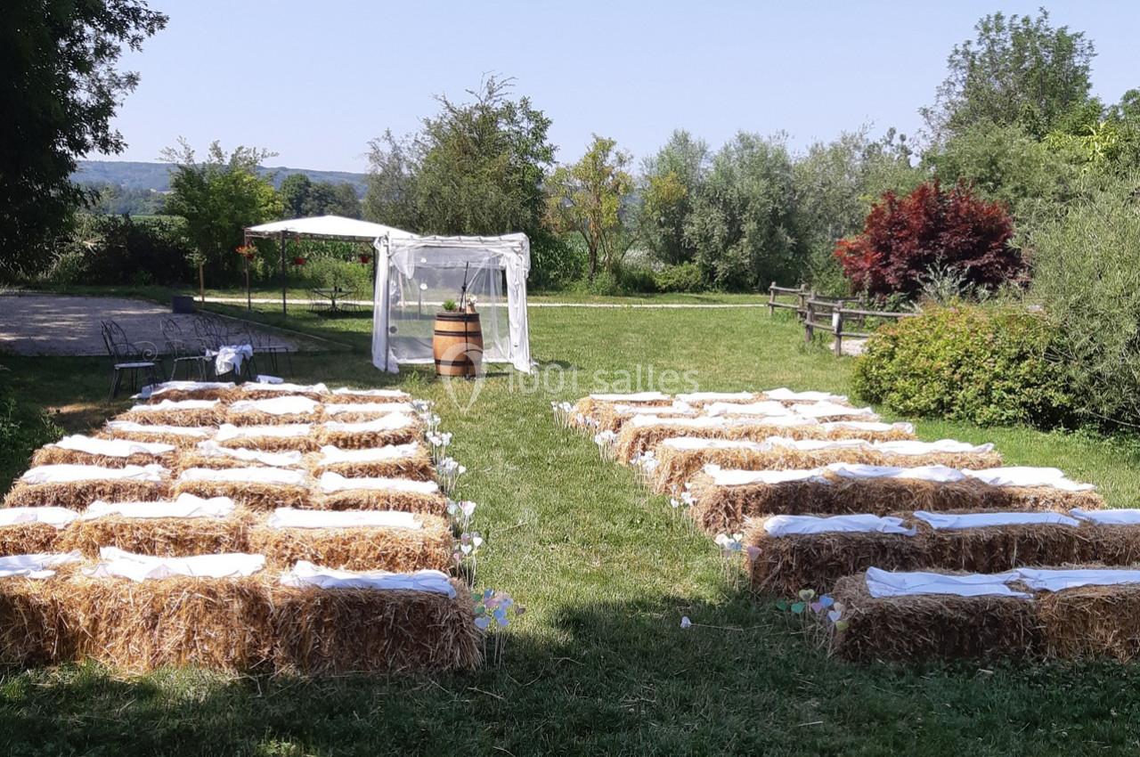Chaises en bottes de paille alignées en extérieur, face à une arche décorée pour une cérémonie champêtre.