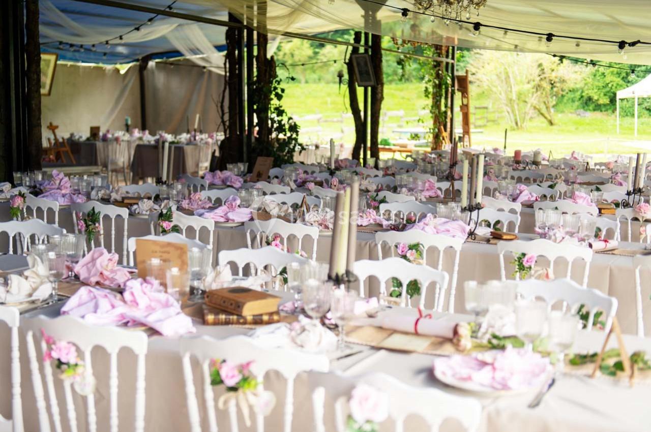 Salle de réception en plein air décorée avec des tables nappées, des chaises blanches et des détails floraux roses.