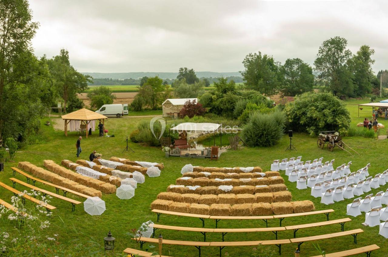 Disposition d'une cérémonie en plein air avec bottes de paille en guise de sièges et allée centrale, entourée de verdure.