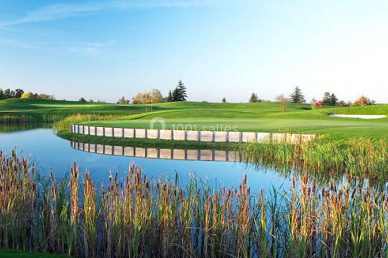 Plan d'eau entouré de roseaux devant un terrain de golf verdoyant sous un ciel dégagé.