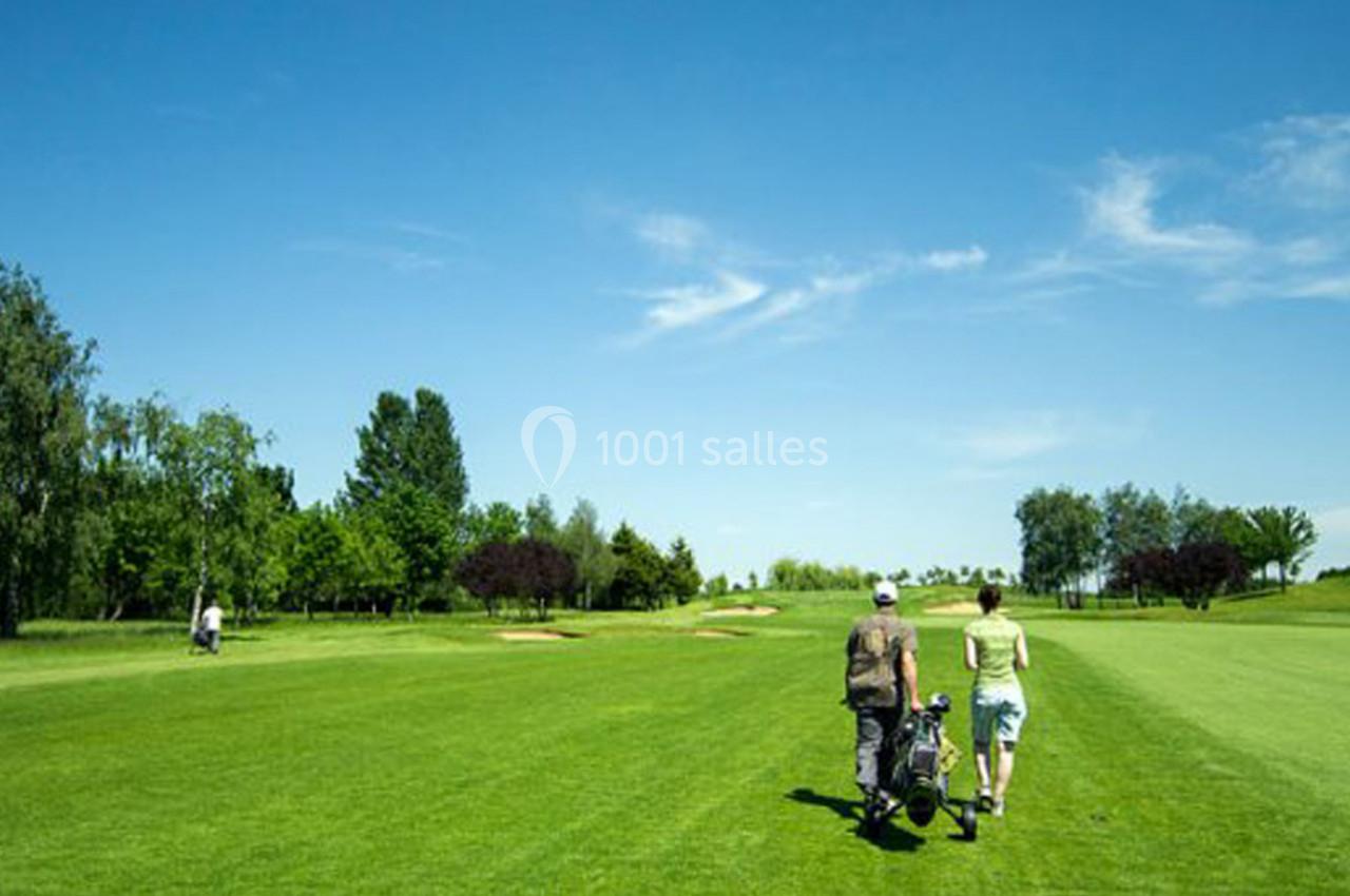 Deux personnes marchent sur un parcours de golf verdoyant sous un ciel bleu dégagé, avec des arbres en arrière-plan.