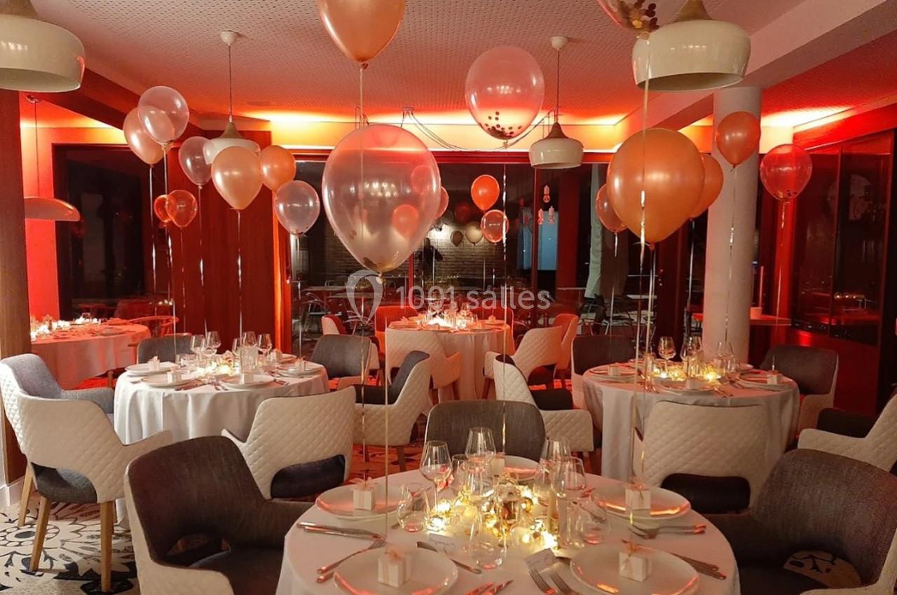 Salle de réception décorée avec des ballons et des tables dressées pour un événement festif en soirée.