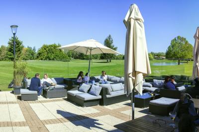 Paysage de golf avec pelouses verdoyantes, reliefs ondulés et maisons en arrière-plan sous un ciel dégagé.