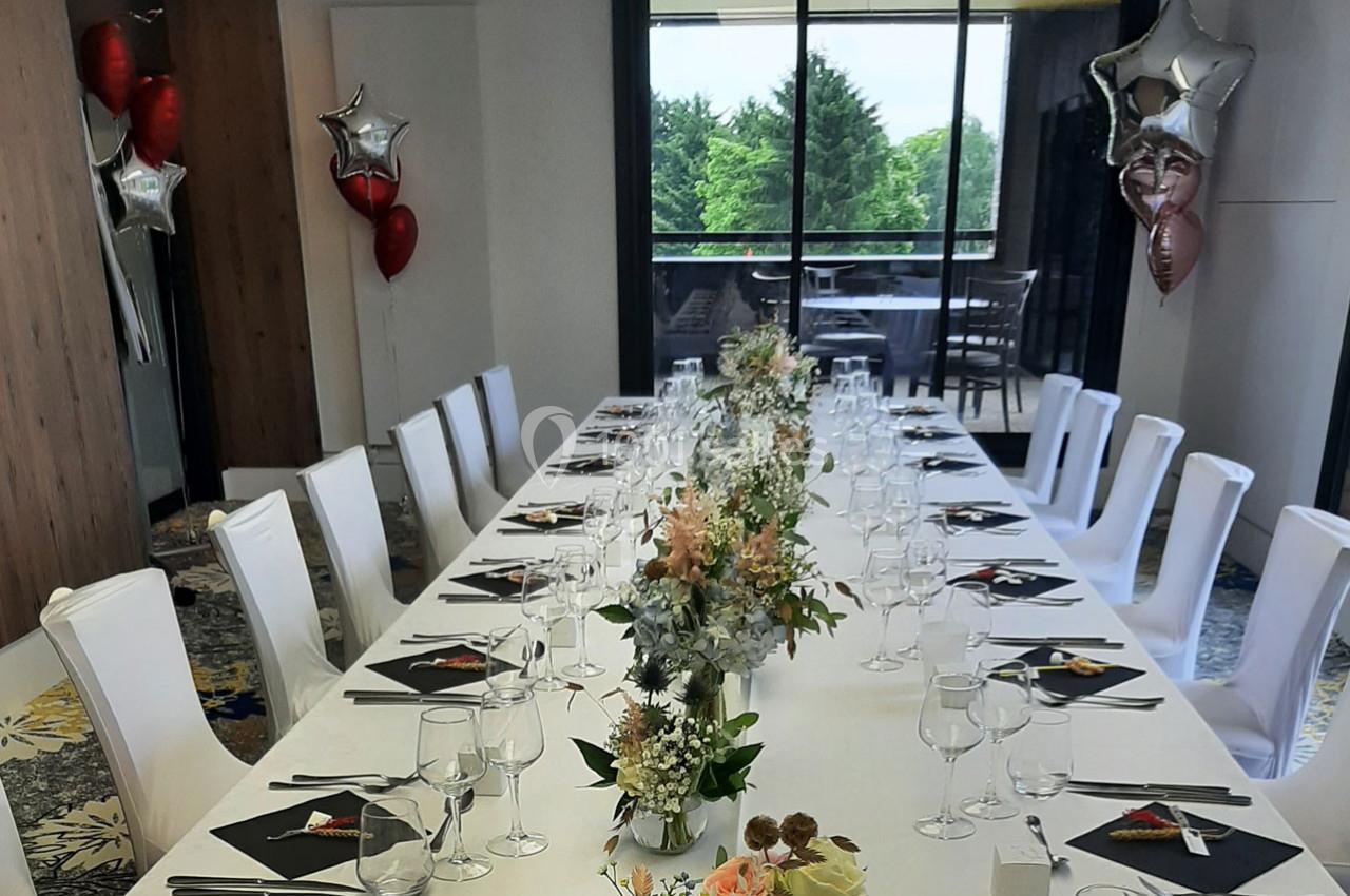 Table dressée pour un repas festif, décorée de fleurs et entourée de chaises blanches, avec des ballons en arrière-plan.