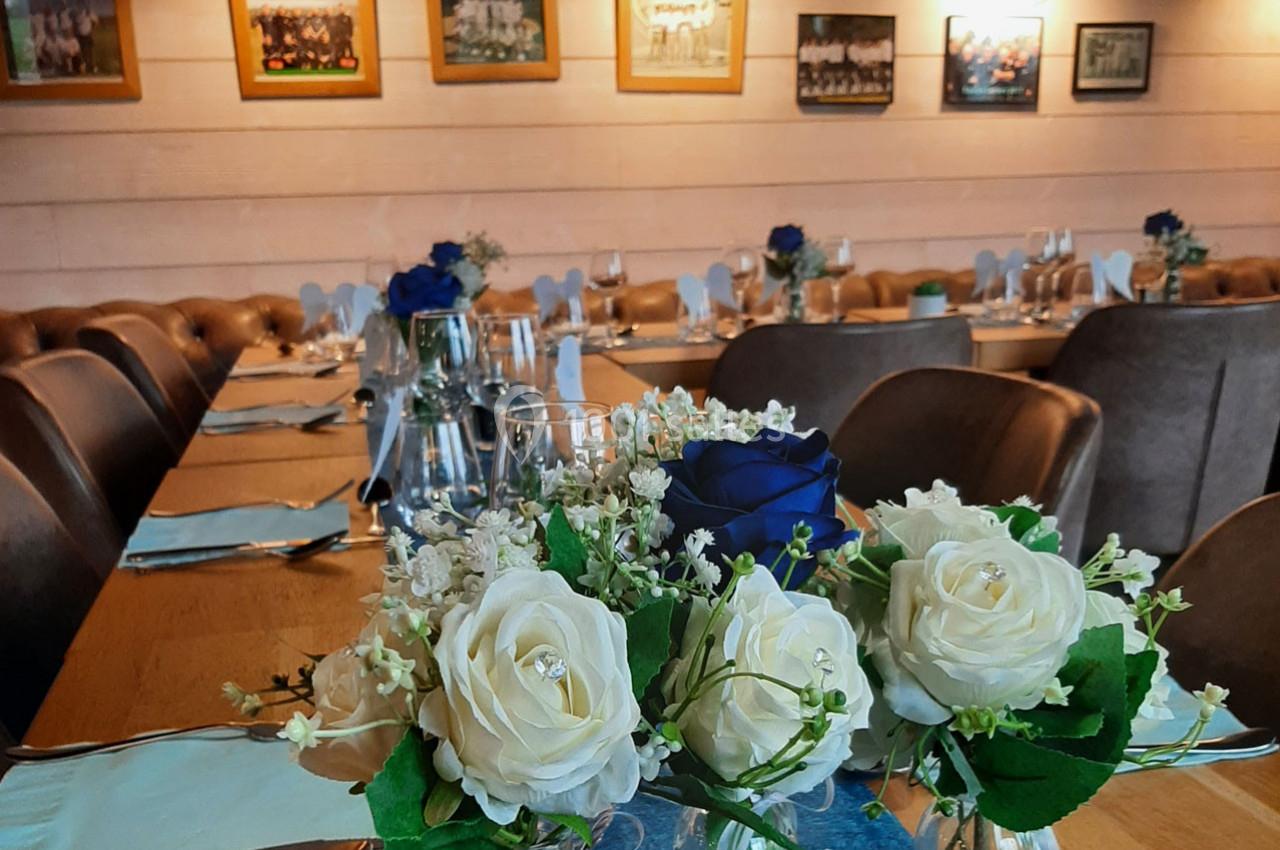 Salle de réception décorée avec des roses blanches et bleues sur une table dressée, entourée de chaises en cuir.