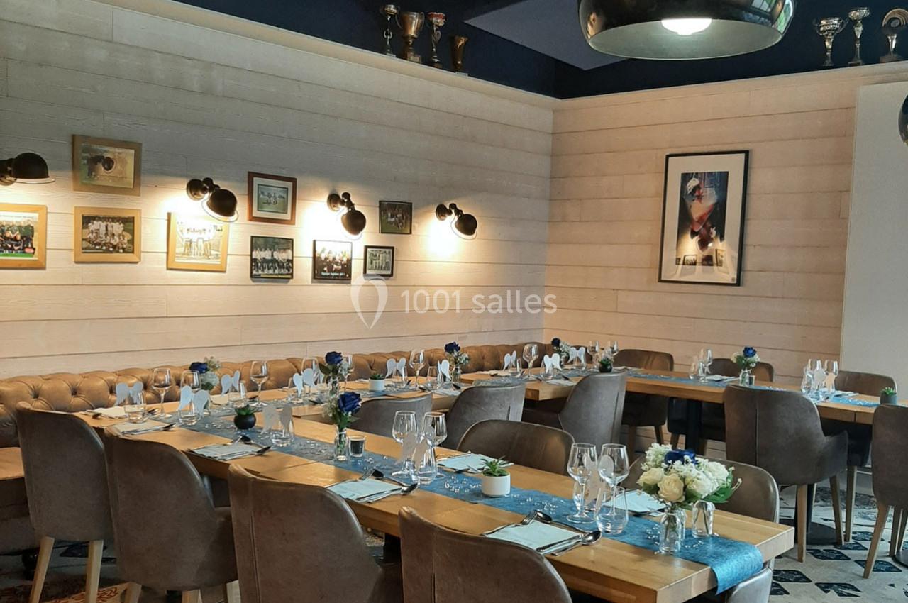 Salle de restaurant élégante avec tables dressées, décorée de cadres, trophées et éclairée par des appliques murales.