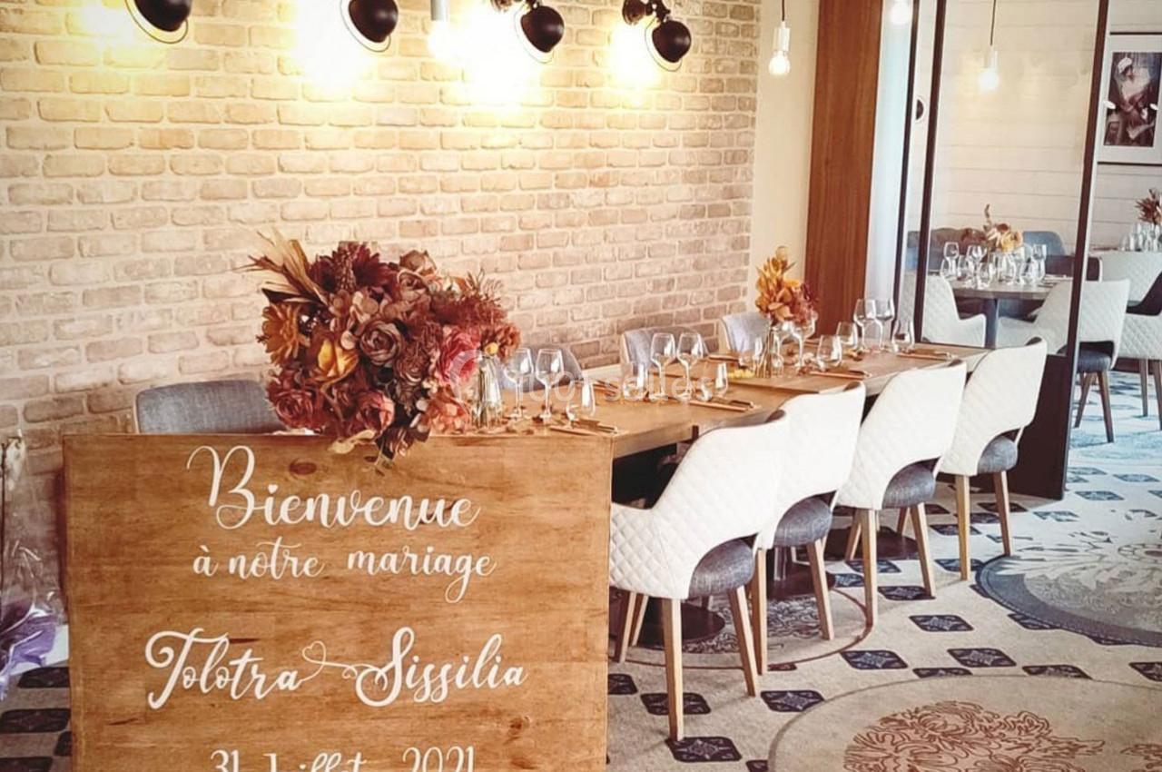 Salle de réception décorée pour un mariage avec une table dressée et un panneau en bois accueillant les invités.