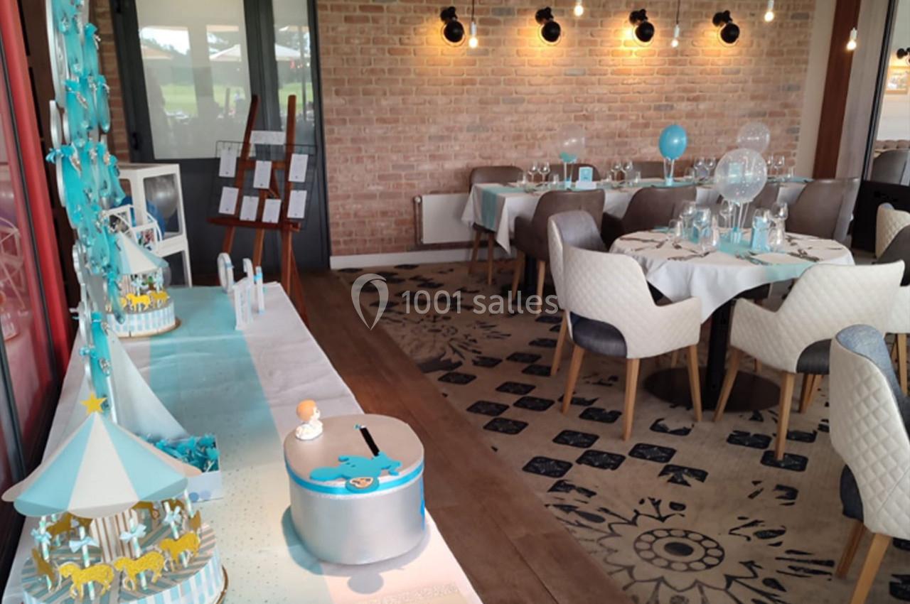 Salle décorée pour une fête avec tables dressées, guirlandes lumineuses et une table de buffet à thème bleu et blanc.