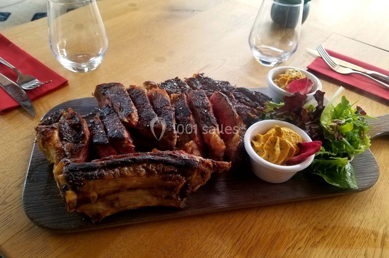 Planche de côtes de bœuf grillées accompagnée de salade verte et de deux ramequins de sauce sur une table en bois.