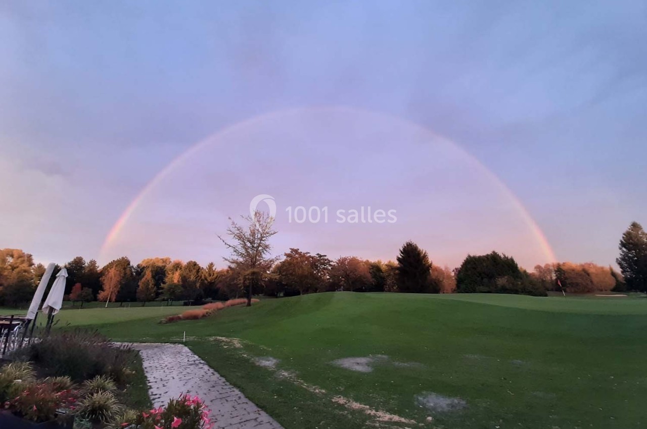 Un arc-en-ciel complet au-dessus d'un terrain de golf verdoyant entouré d'arbres sous un ciel nuageux.