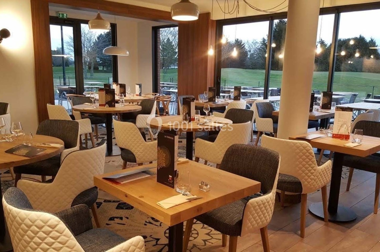 Salle de restaurant lumineuse avec tables en bois, chaises rembourrées et grandes baies vitrées donnant sur un espace…