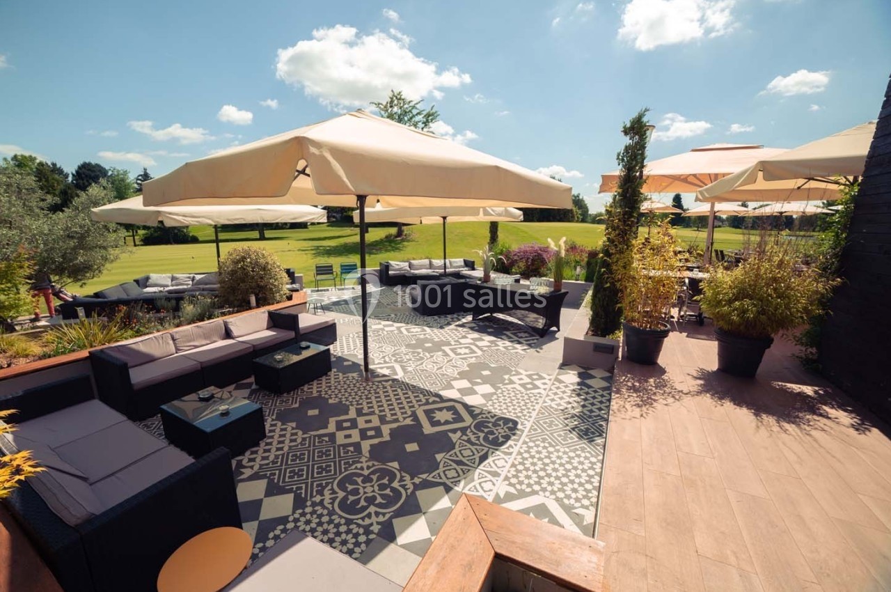 Terrasse aménagée avec canapés, tables basses, grands parasols et vue sur un jardin verdoyant par temps ensoleillé.