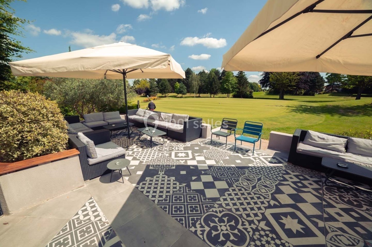 Terrasse aménagée avec mobilier de jardin, parasols et vue sur un grand espace vert parsemé d'arbres.