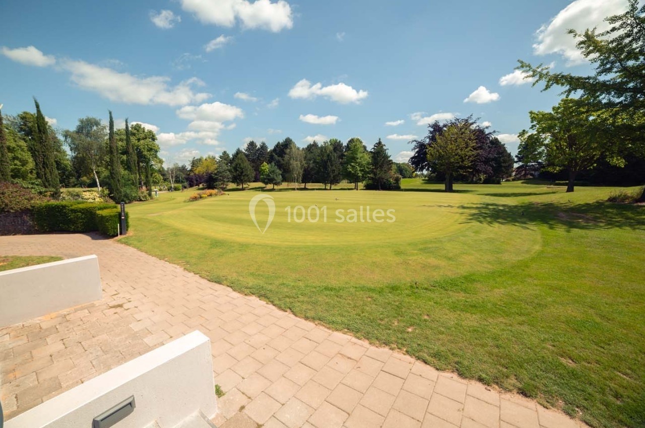 Pelouse bien entretenue avec un chemin pavé au premier plan, entourée d'arbres sous un ciel bleu parsemé de nuages.