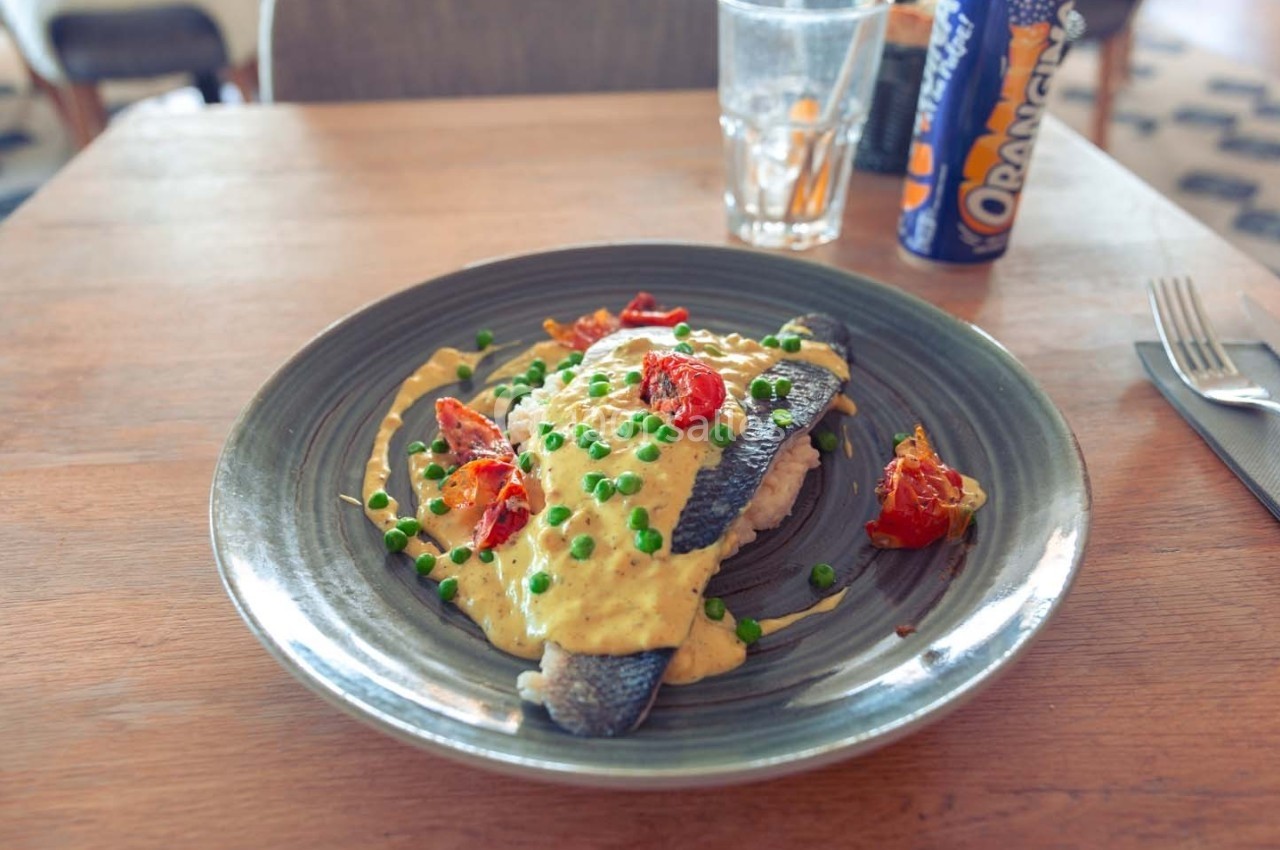 Plat de poisson servi avec une sauce crémeuse, des petits pois et des tomates rôties, accompagné d'une boisson gazeuse.
