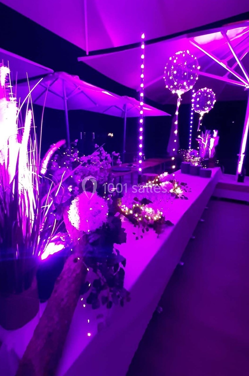 Décoration lumineuse violette avec fleurs, guirlandes et parasols éclairés dans un espace intérieur sombre.