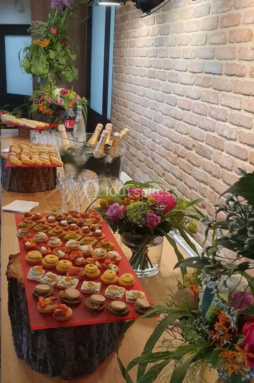 Plateau de bouchées apéritives variées sur une table en bois décorée de fleurs et de bouteilles de champagne.