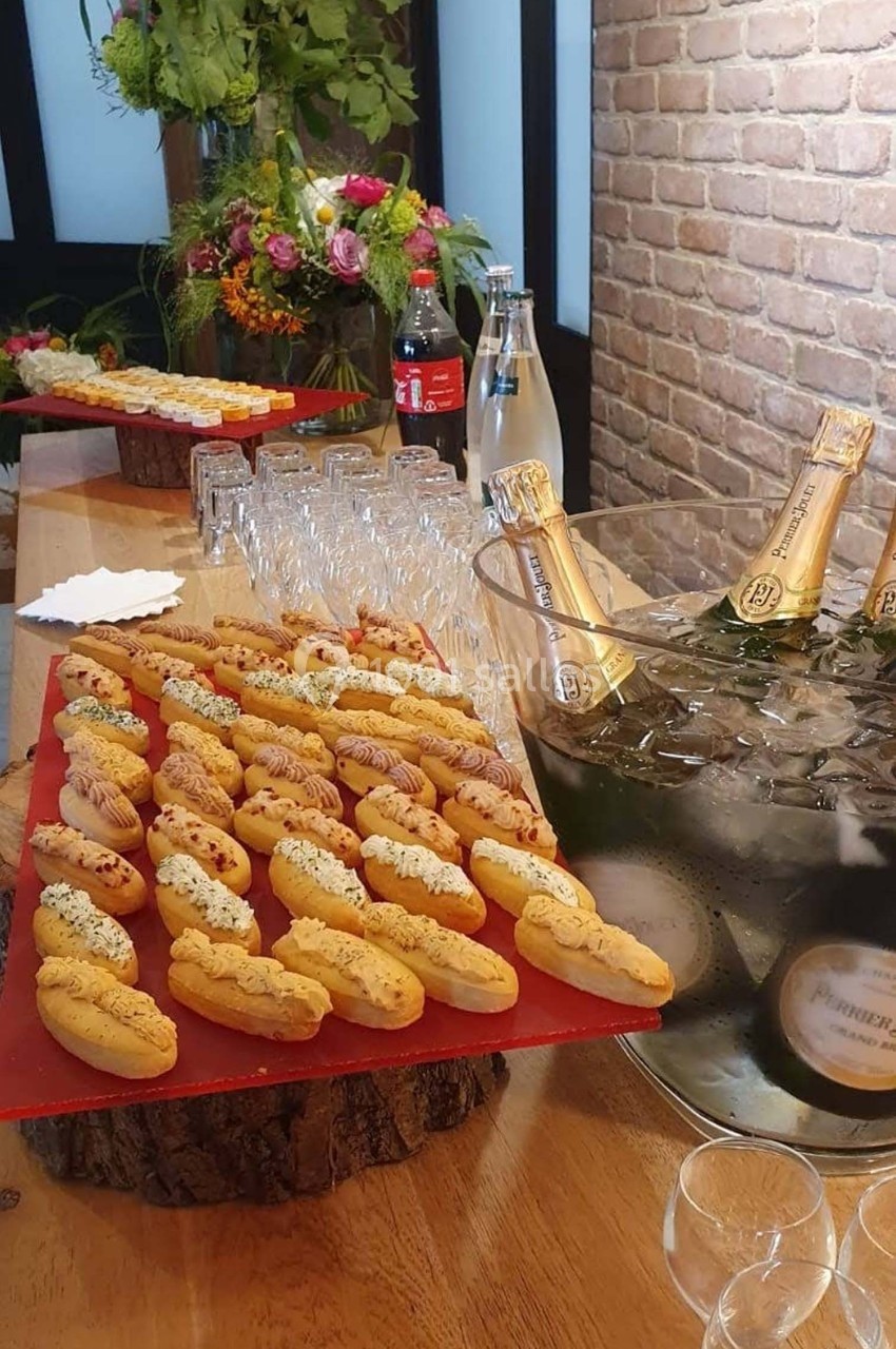 Plateau d'éclairs salés disposés sur une table avec des bouteilles de champagne dans un seau de glace en arrière-plan.