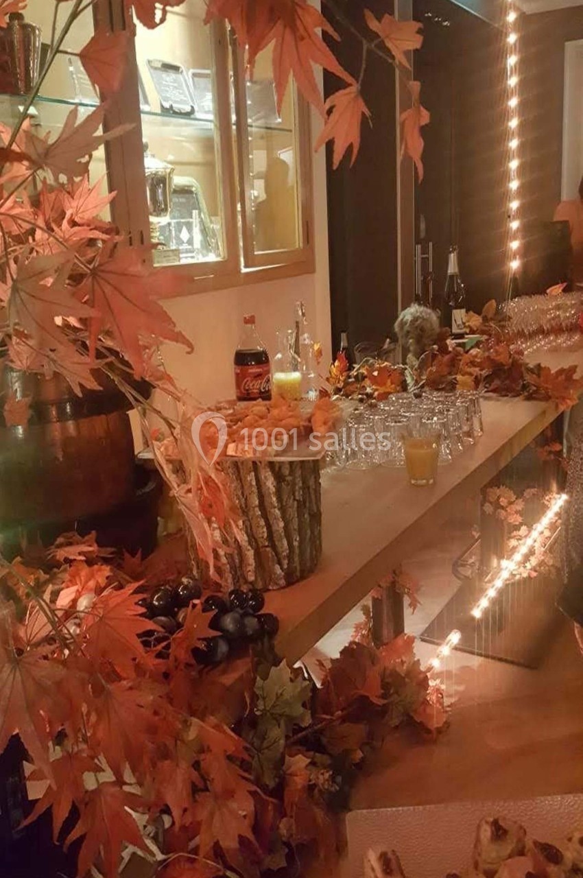 Table décorée sur le thème de l'automne avec feuilles rouges, boissons, verrerie et amuse-bouches dans un cadre chaleureux.