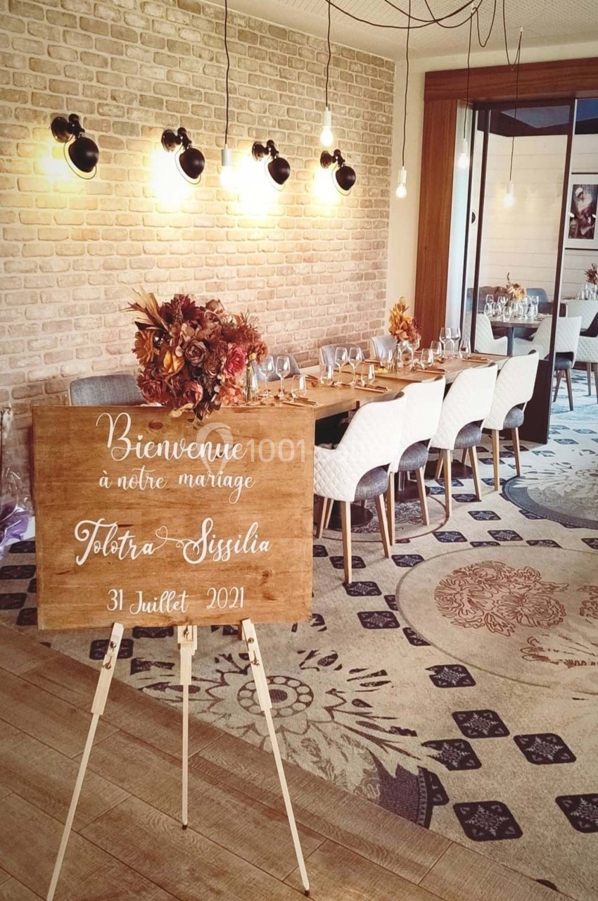 Panneau de bienvenue pour un mariage devant une table décorée, dans une salle lumineuse au style chaleureux.