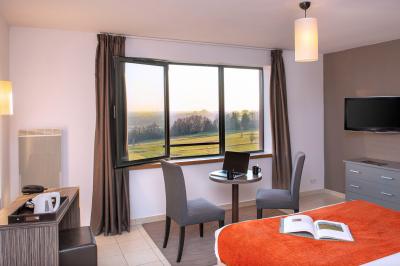 Vue d'un terrain de golf verdoyant avec des arbres et une ville en arrière-plan sous un ciel dégagé.