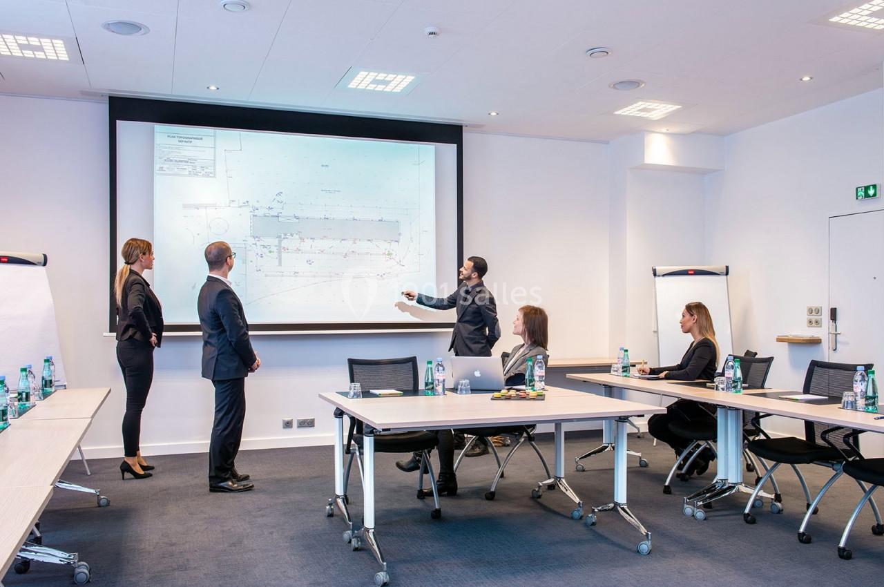 Un groupe de personnes en réunion dans une salle, regardant une présentation projetée sur un écran.