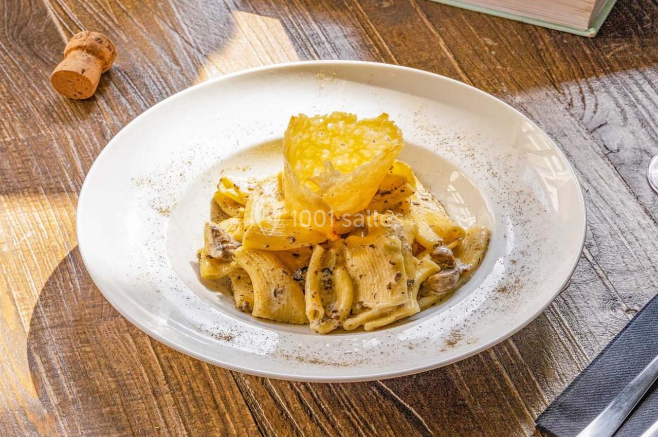 Assiette de pâtes rigatoni à la truffe avec une tuile de parmesan, servie sur une table en bois.