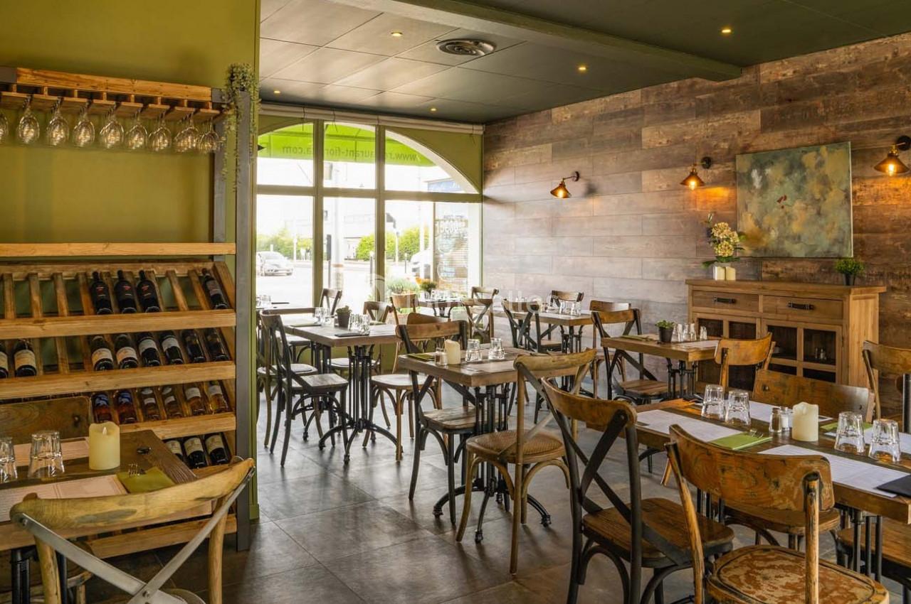 Salle de restaurant lumineuse avec tables en bois, chaises assorties, étagères à vin et décoration murale chaleureuse.