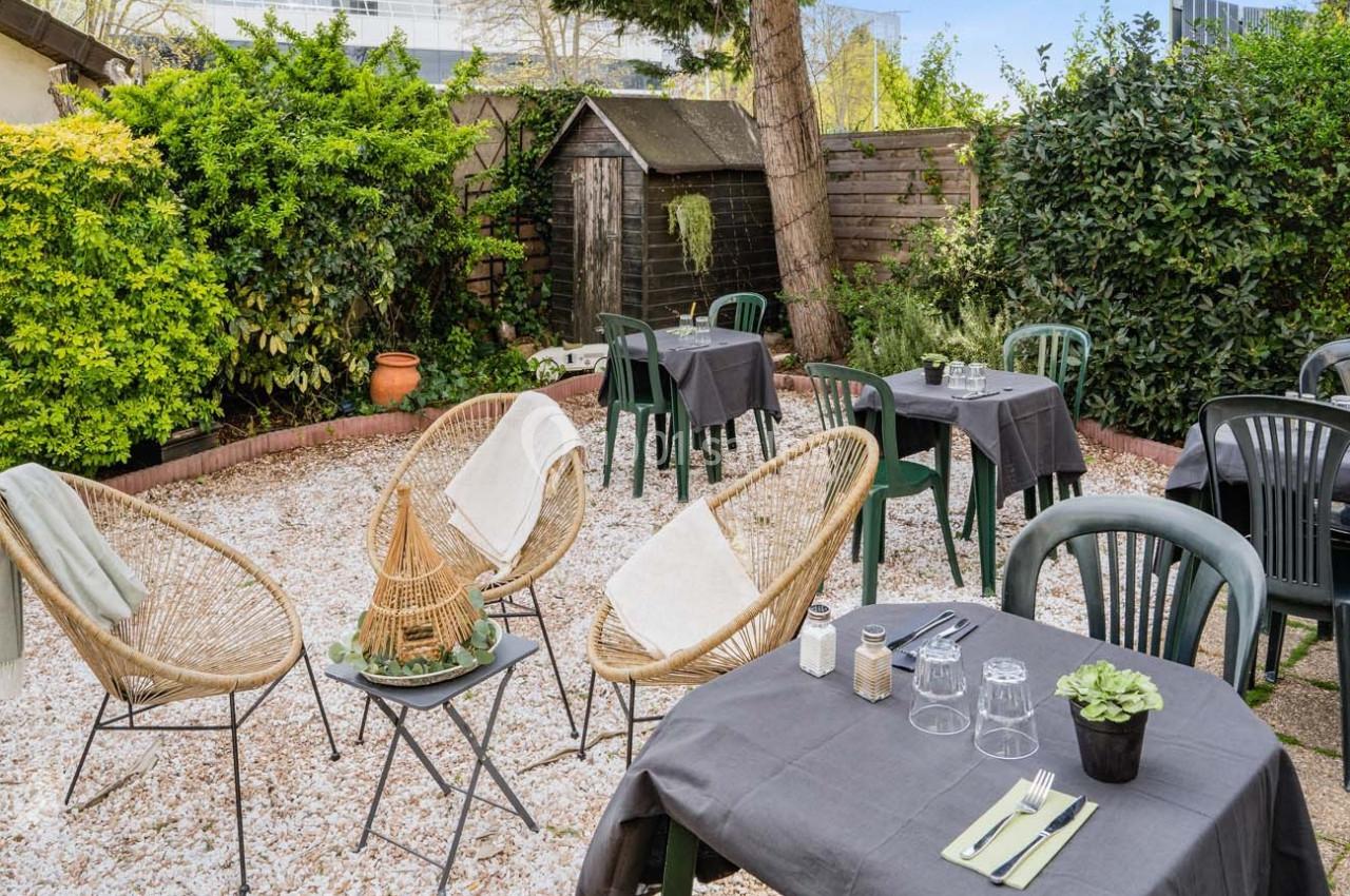 Tables dressées avec nappes grises et chaises disposées dans un jardin extérieur entouré de verdure.
