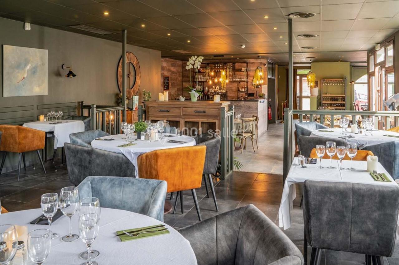 Salle de restaurant élégante avec tables dressées, chaises colorées et bar en bois au fond.
