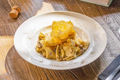 Assiette de pâtes rigatoni à la truffe avec une tuile de fromage, servie sur une table en bois.