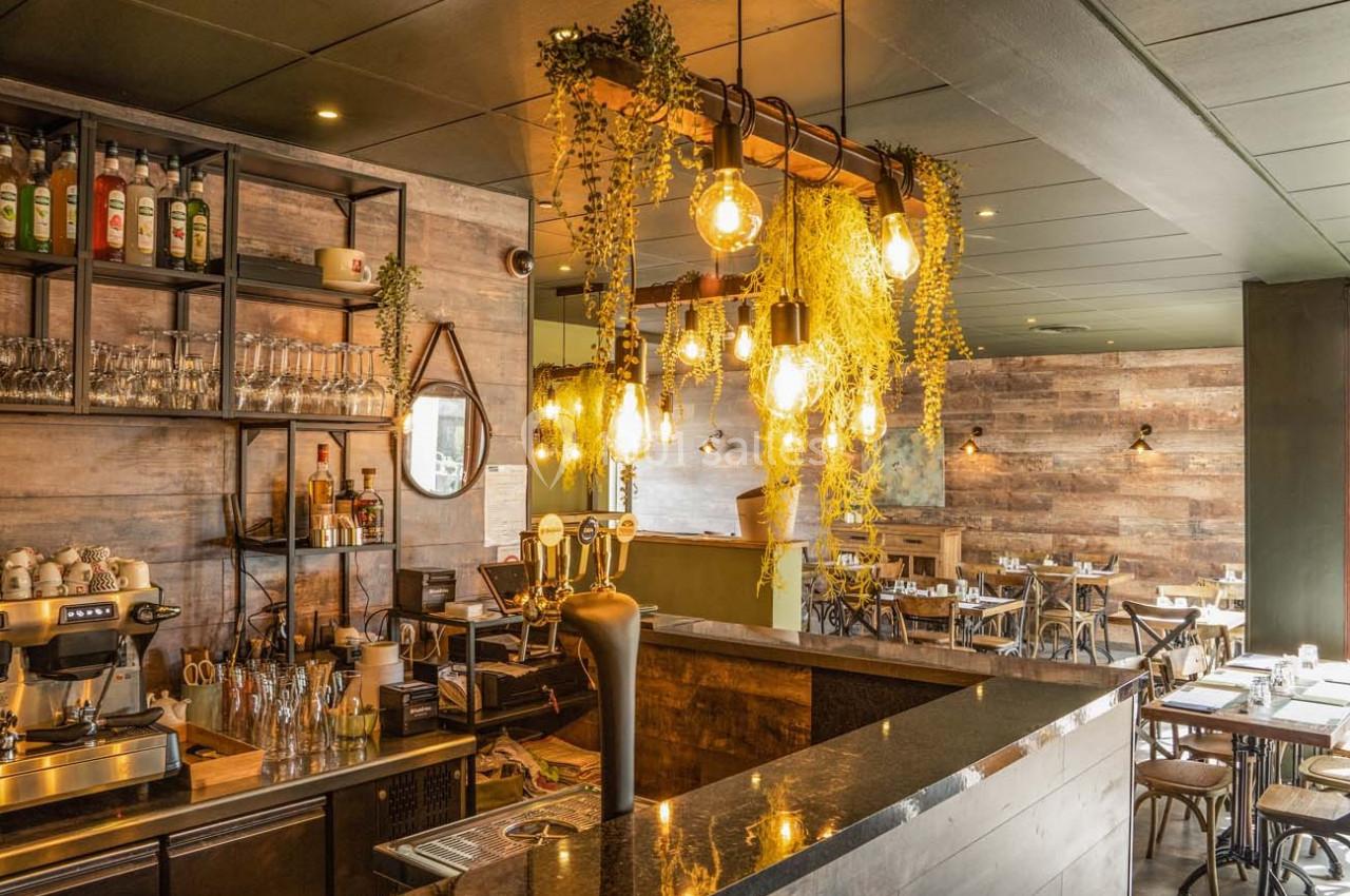 Intérieur d'un café-restaurant avec un bar en bois, des luminaires suspendus et une décoration végétale.