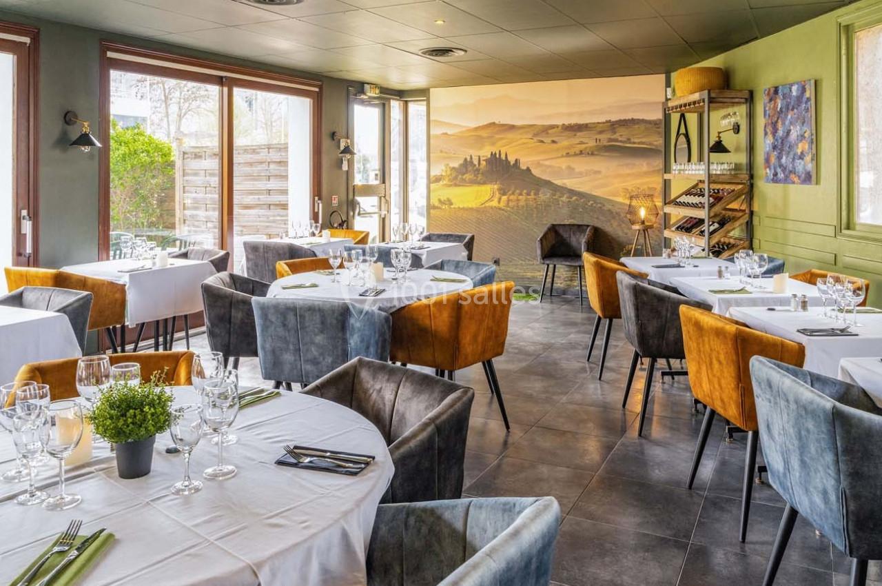 Salle de restaurant lumineuse avec tables dressées, chaises colorées et vue sur une fresque de paysage viticole.
