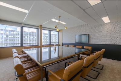 Salle de réunion moderne avec table en marbre, chaises bleues, écran mural et cloison vitrée décorative.