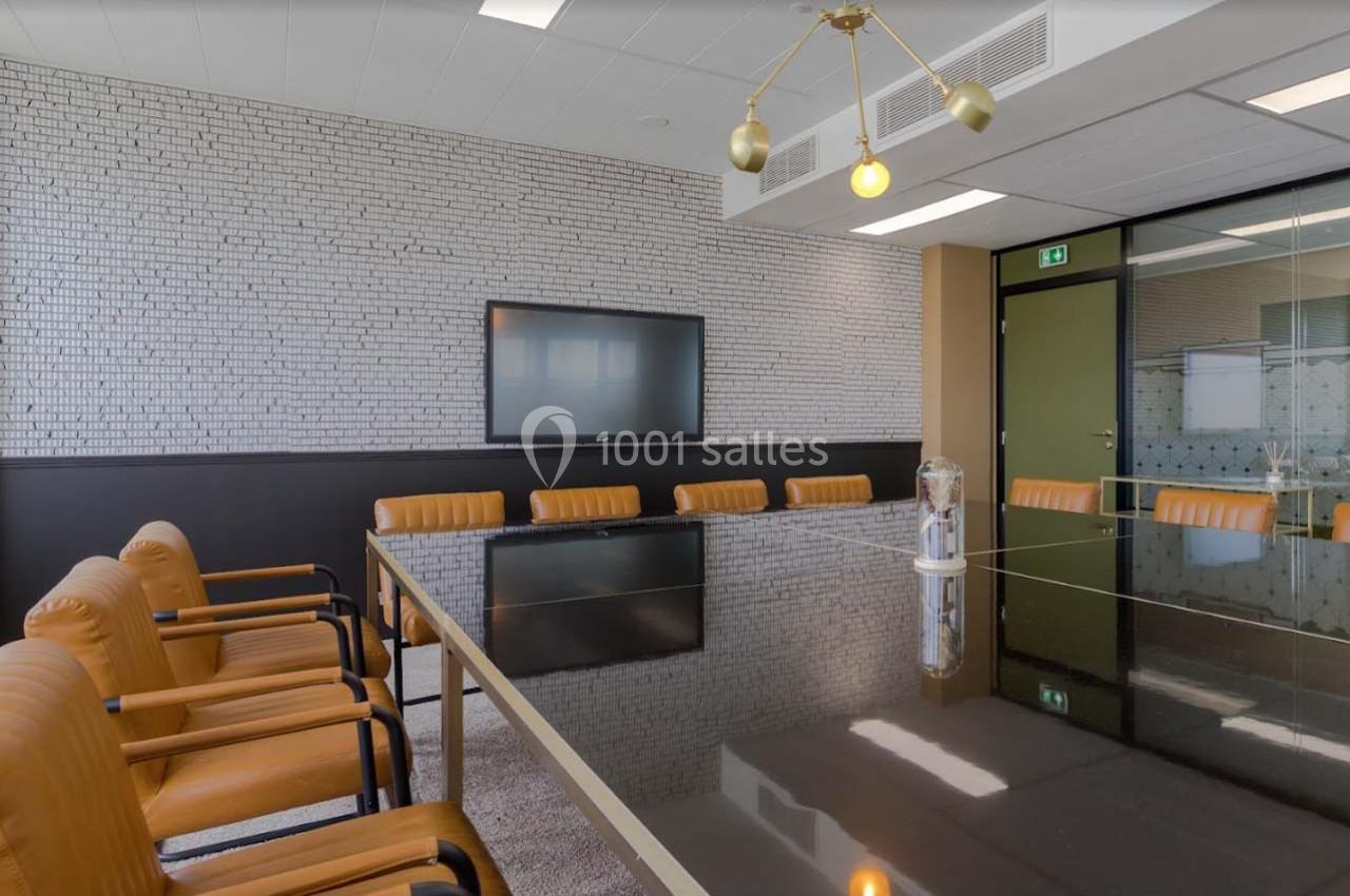 Salle de réunion moderne avec une grande table noire, chaises en cuir marron et écran mural.