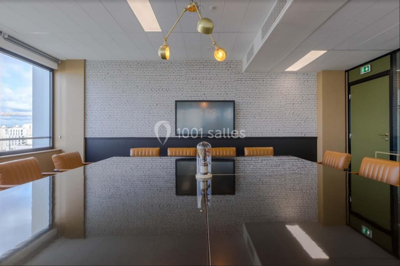 Salle de réunion moderne avec table en bois sombre, chaises en cuir orange, écran mural et éclairage suspendu.