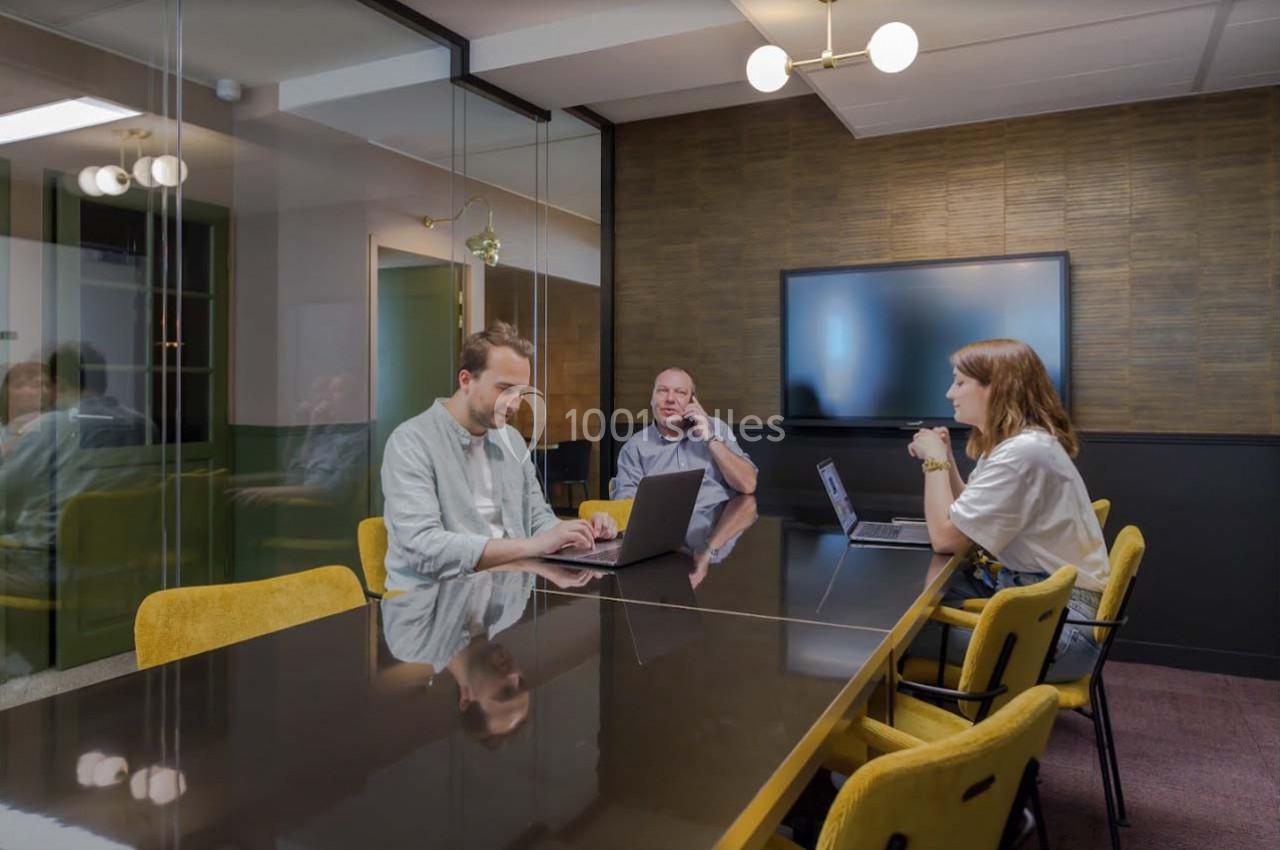 Trois personnes travaillent sur des ordinateurs portables dans une salle de réunion moderne avec une grande table et un…